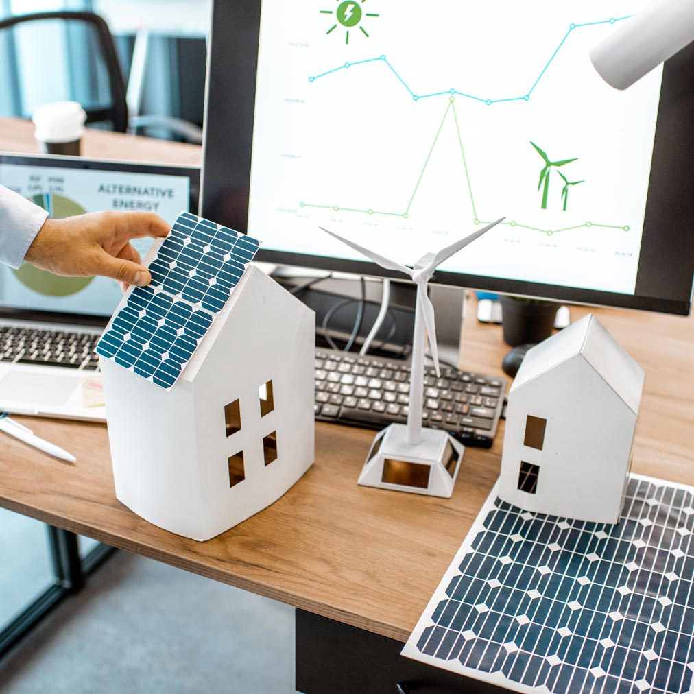 Hausmodelle mit Solaranlagen auf einem Planungstisch mit Computer
